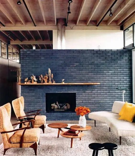 a bold mid-century modern living room with a navy brick fireplace and a mantel, some elegant chairs, a daybed and some coffee tables