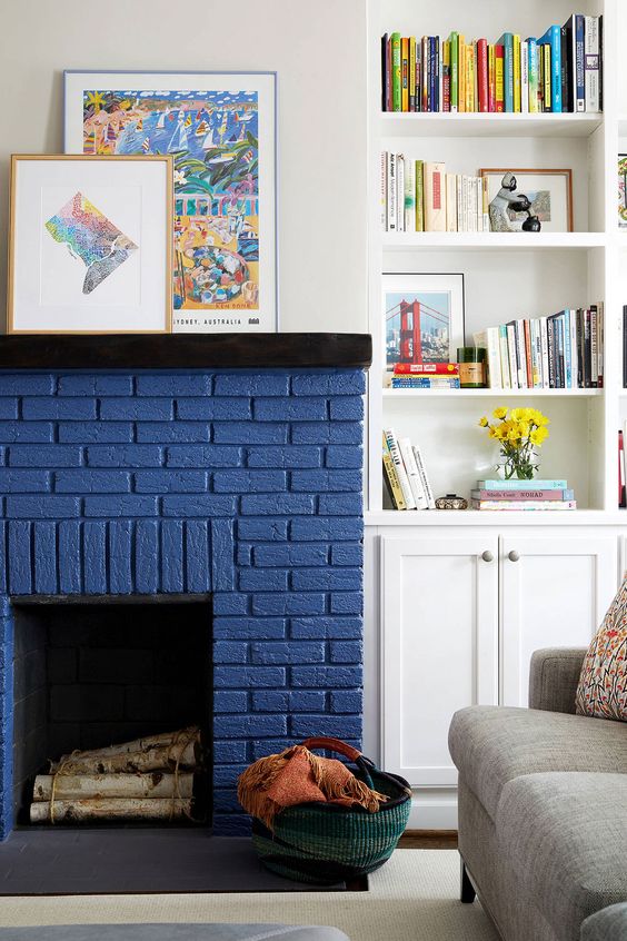 a chic modern living room with a grey sofa, a navy brick fireplace, built-in shelves and a cabinet and some bold artwork