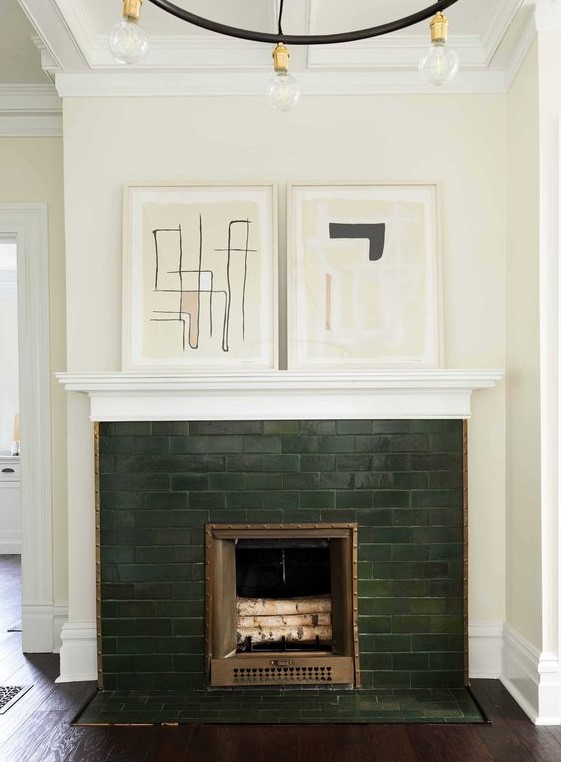 a hunter green brick fireplace with copper detailing and abstract artworks on the mantel looks very elegant and refined