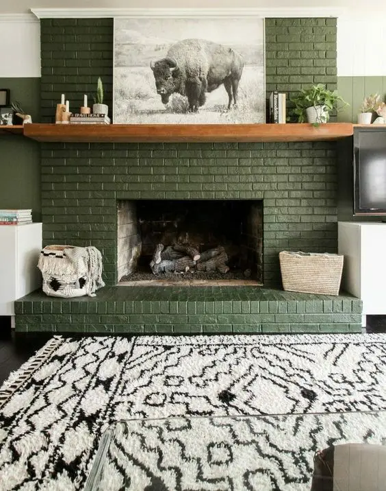 a lovely green brick fireplace with a stained mantel and lovely decor, a printed rug is a cool and cozy boho space
