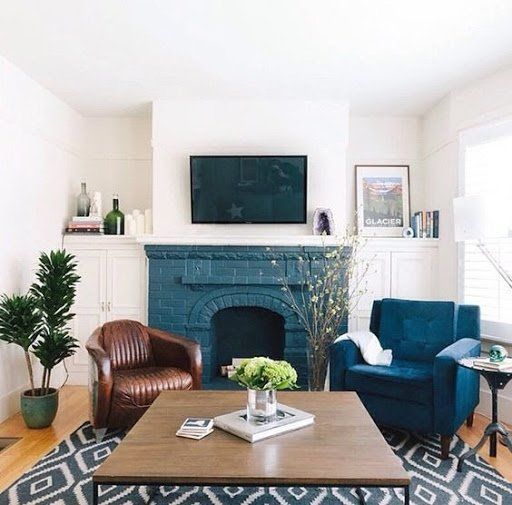 A mid century modern living room with a blue brick fireplace, a brown leather chair and a navy one, a coffee table and some decor