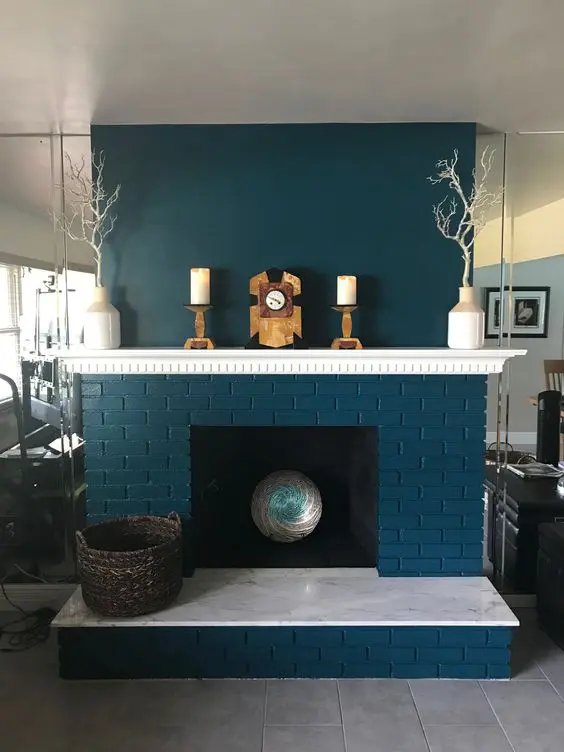 a teal brick fireplace with a chic mantel and some decor, with branches in vases and a basket is a bold and cool decoration