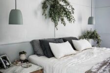 a Scandinavian bedroom with light grey walls, a bed with neutral bedding, nightstands, potted greenery and light green pendant lamps