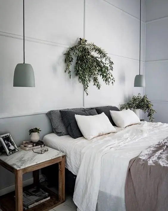 a Scandinavian bedroom with light grey walls, a bed with neutral bedding, nightstands, potted greenery and light green pendant lamps