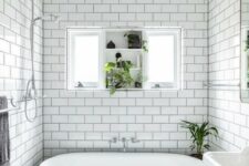 a beautiful black and white bathroom with white subway and black hex tiles, a free-standing sink, a black vintage bathtub and a window