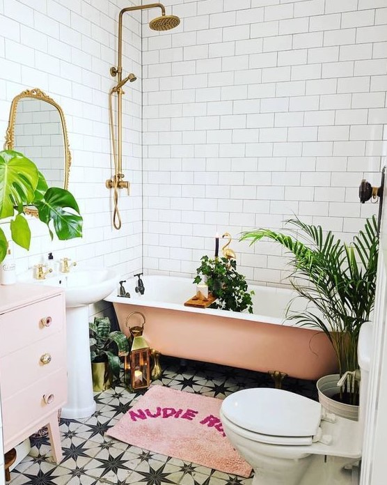 A beautiful tropical bathroom with white subway and black and white star tiles, a peachy pink bathtub, a blush vanity and a free standing sink