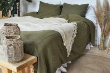 a boho bedroom in neutrals, with a bed done with olive green bedding, a wooden bench and woven candleholders, pampas grass, potted plants and burst mirrors