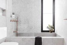 a contemporary bathroom clad with concrete and marble hex tiles, a tub clad with concrete tiles, white appliances and cropped fixtures