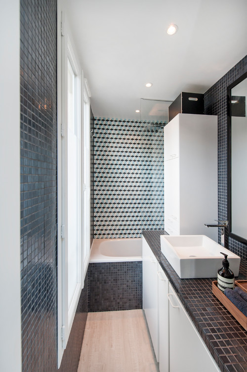 a contemporary black and white bathroom with a tub, some cabinetry, a window and cool tiles in the tub zone
