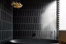 a contemporary black bathroom clad with skinny tiles, a terrazzo floor, a glazed wall and a cluster of pendant lamps