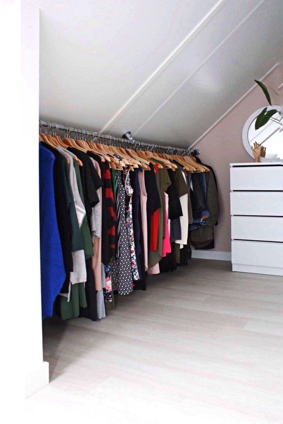 a cool attic closet wiht a pink accent wall, a white dresser, a rail with clothes is a very smart idea for a small home with an attic