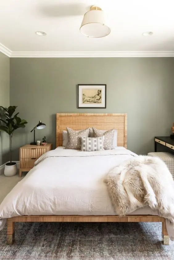 a cool guest bedroom with green grey walls, a  wooden bed with neutral bedding, a wooden nightstand and a black vanity