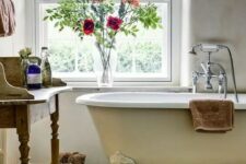 a country bathroom with neutral walls, a neutral clawfoot bathtub, a wooden vanity and blooms and towels
