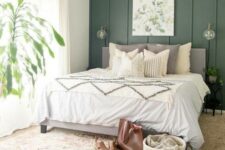 a cozy farmhouse bedroom with a green accent wall, a grey bed with neutral bedding, a printed rug, potted greenery and an artwork