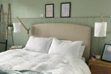 a lovely sage green bedroom with a grey bed and green and white bedding, cane nightstands, a ladder and sconces