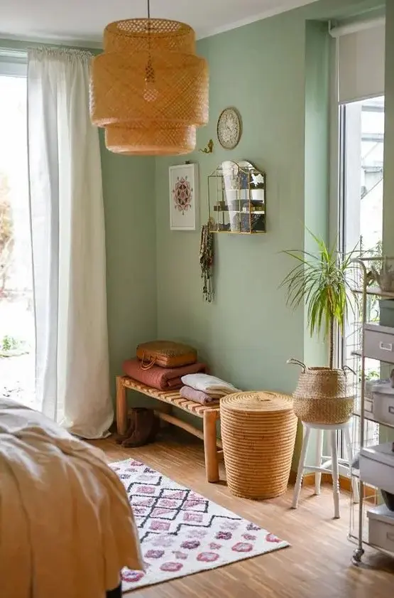 a mint green bedroom with neutral curtains, a woven bench and blankets, a shelving unit, baskets and a woven pendant lamp