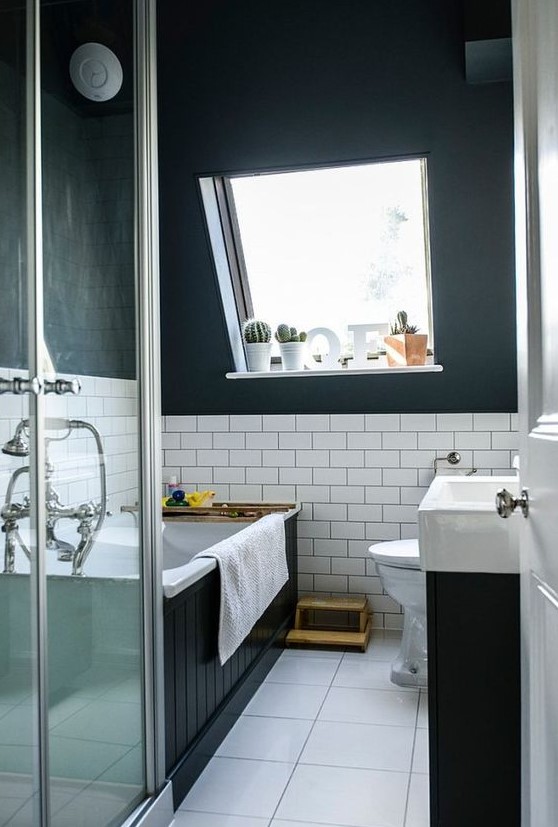 a modern black and white attic bathroom with a bathtub clad with black palnks, a black vanity with a white sink, a square tile floor
