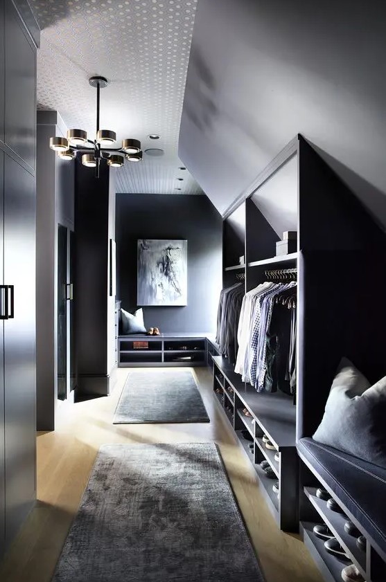 a moody sloped closet with open storage compartments and benches, with rugs and decor plus an elegant chandelier is lovely