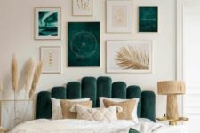 a neutral and forest green bedroom with a bed with an upholstered headboard, a bold gallery wall, a wooden lamp and pampas grass