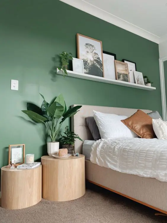 a pretty bedroom with a green accent wall, a neutral bed with neutral bedding, a ledge gallery wall, tree stump side tables
