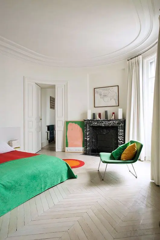 A refined bedroom with a non working fireplace, a bed with green and red bedding, a green chair and a red rug
