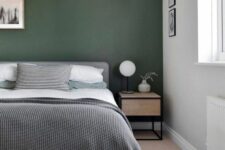 a relaxed modern bedroom with a dark green accent wall, a grey bed with neutral bedding, a printed rug and a stained nightstand