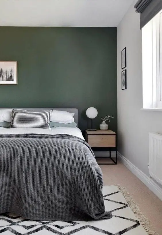 a relaxed modern bedroom with a dark green accent wall, a grey bed with neutral bedding, a printed rug and a stained nightstand