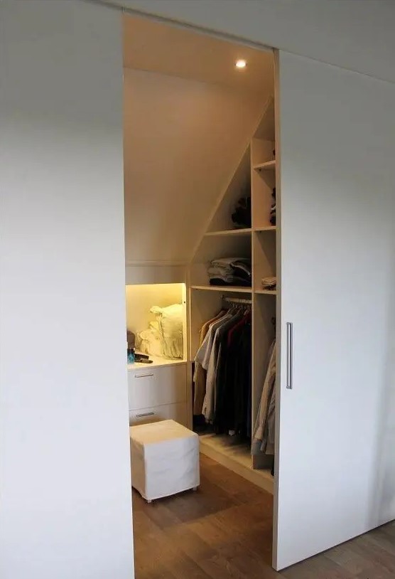 A small attic closet with open storage compartments and niches, with drawers and shelves, built in lights and sliding doors