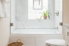 a small modern bathroom with marble tiles, a white tub, marble herringbone tiles, a sink and a basket