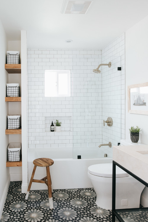 a stylish modern bathroom with white subway and printed tiles, a sink on a stand, a white tub and a wooden stool