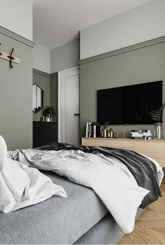 a stylish modern bedroom with sage green walls, an upholstered grey bed with grey bedding, a stained dresser and a black one