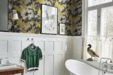 a vintage bathroom with moody floral wallpaper, creamy paneling, a free-standing bathtub, black and white tile floor and a vintage vanity