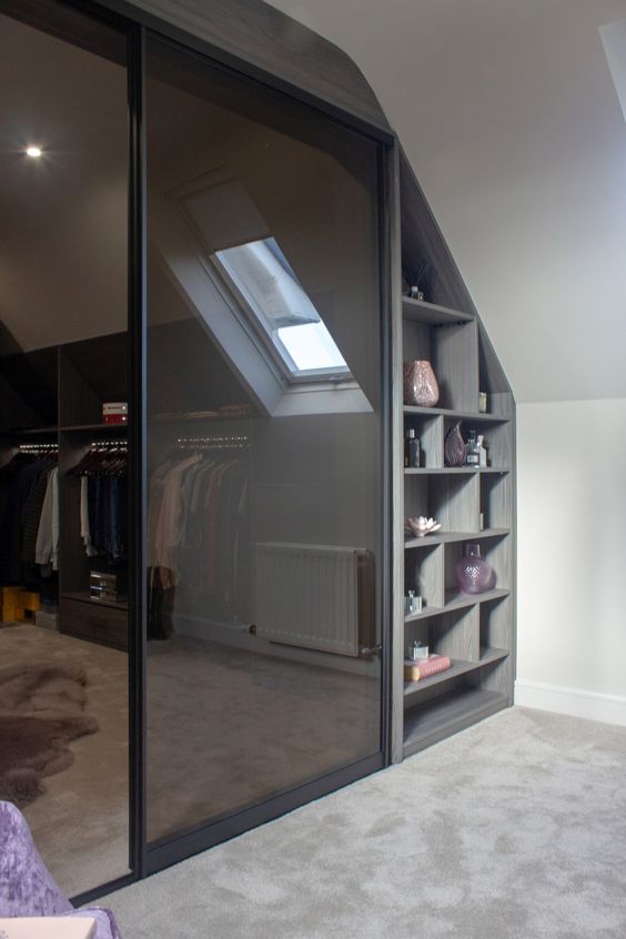 A walk in closet with a slanted ceiling, with railings, shelves and smoked glass doors is a perfect modern idea