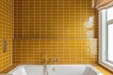 a warm yellow bathroom fully clad with tiles, bright printed textiles, a basket with a lid for storage and a window with frosted glass
