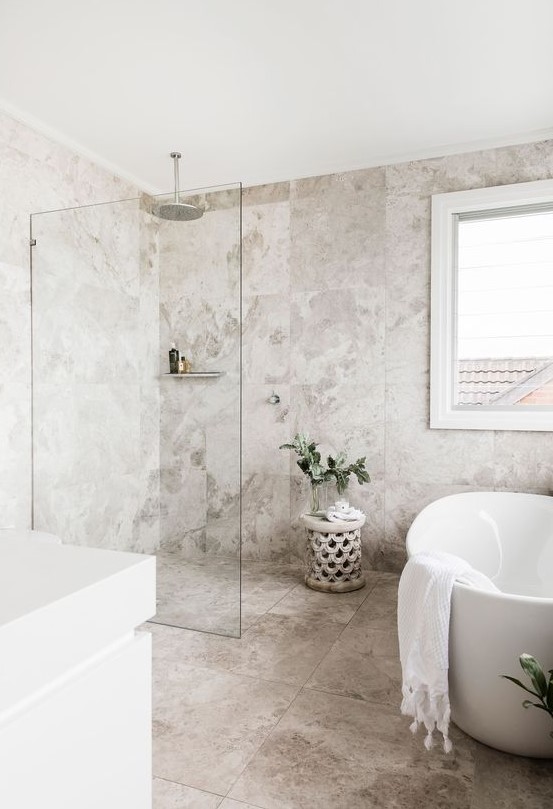 a welcoming neutral bathroom with catchy stone tiles, white appliances and a vanity and some greenery in vases