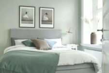 an airy Scandinavian bedroom with sage green walls, a grey upholstered bed with green and neutral bedding, a printed rug