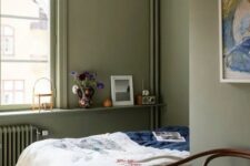 an olive green bedroom with a bed and colored bedding, a paper pendant lamp and a windowsill with decor