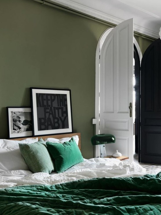 an olive green bedroom with a bed and emerald bedding, a mini gallery wall and a cool table lamp in green