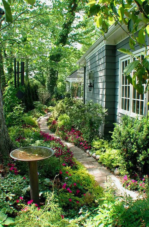 a whimsical fairy garden with greenery and bright blooms, trees and a stone path plus a bird bath is gorgeous