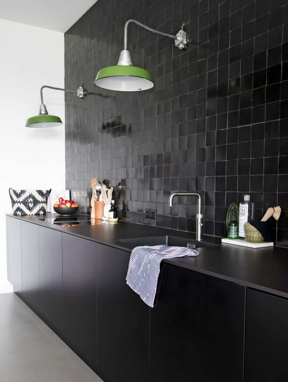 a black glazed tile backsplash, stone countertops and sleek black cabinets plus green wall lamps