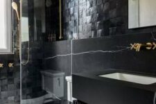 13 a modern moody bathroom with catchy tiles and black marble, a floating vanity, gold fixtures and a mirror