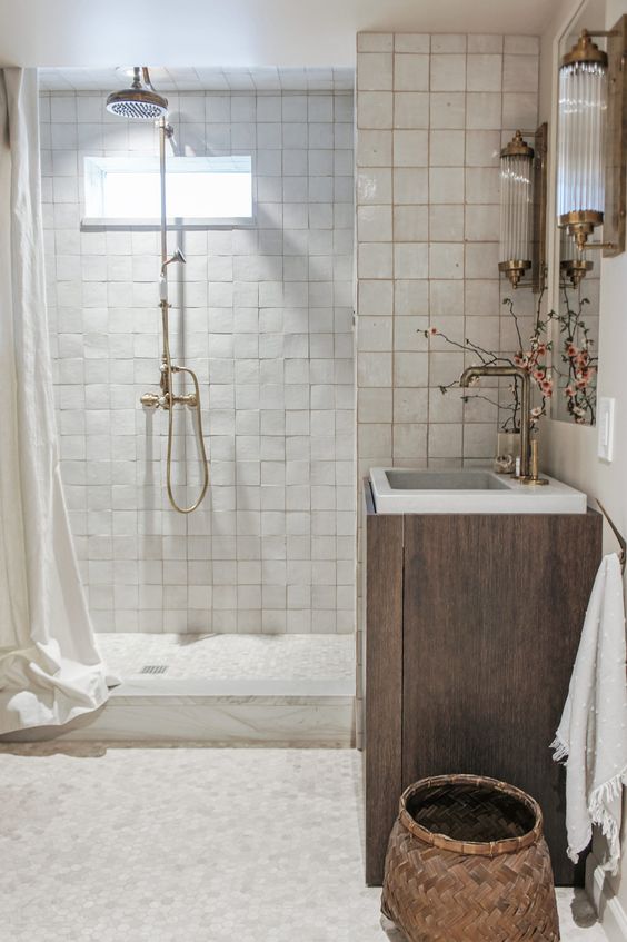 a neutral bathroom clad with neutral zellige tiles, a timber vanity, a mirror, some lovely vintage sonces and a basket