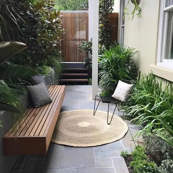 a small townhouse side yard with stone tiles, a built-in bench, hairpin leg furniture and potted greenery with much texture