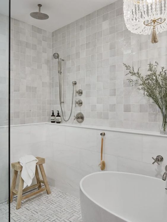 a neutral bathroom clad with zellige tiles and geo ones on the floor, an oval tub and a shower, some greenery