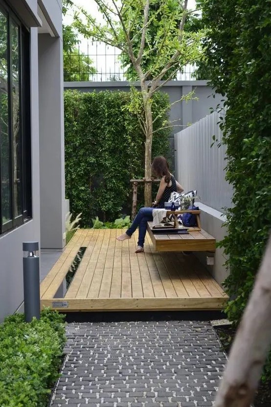 a small modern side yard with a deck and a floating bench plus greenery walls and a tree for relaxing outside