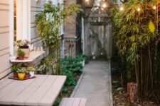 19 a side yard with a concrete path, a wooden dining set, bamboo and greenery and string lights