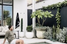 23 a chic black and white outdoor space with a white stone deck and a pool, potted plants and cacti, a bench with pillows