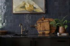 23 a moody kitchen with black cabinets, a navy zellige tile backsplash, a grey marble countertop and brass and gold fixtures