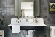 24 a vintage bathroom with grey zellige tiles, a black floating sink, a curved mirror, brass and gold fixtures and marble tile on the floor