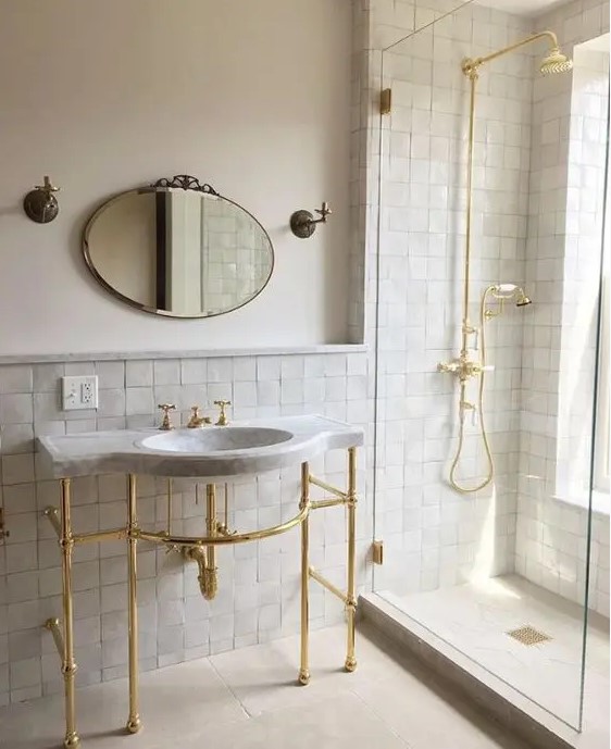 An elegant neutral bathroom accented with neutral zellige tiles, with a free standing sink and gold fixtures